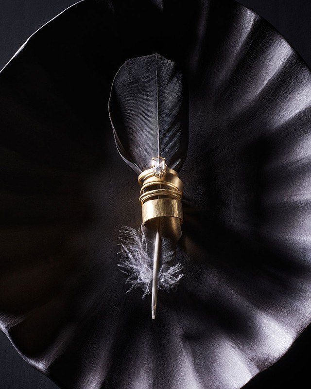 Close-up of gold jewelry rings stacked on a quill with white and black feathers against a dark rippled surface. 