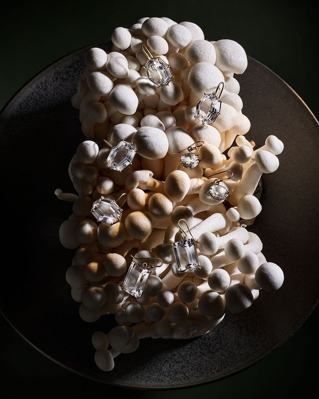 Elegant still life showcasing white mushrooms arranged in a textured bowl, adorned with a selection of shiny jewel earrings.