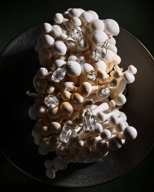 Elegant still life showcasing white mushrooms arranged in a textured bowl, adorned with a selection of shiny jewel earrings.