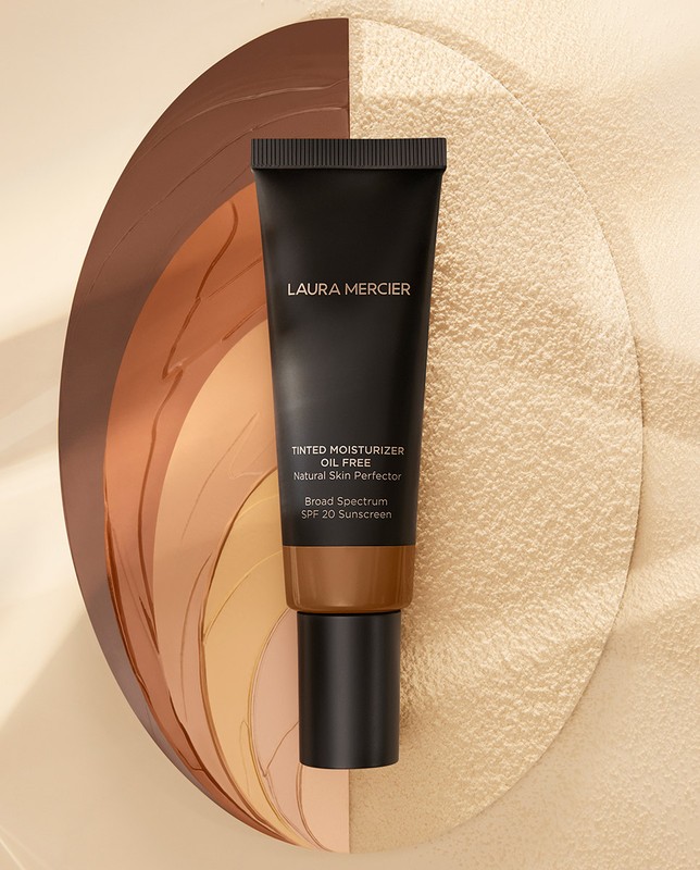 Laura Mercier tinted moisturizer SPF 20 in dark packaging against a beige backdrop. Beauty product photo, skincare, sunscreen.