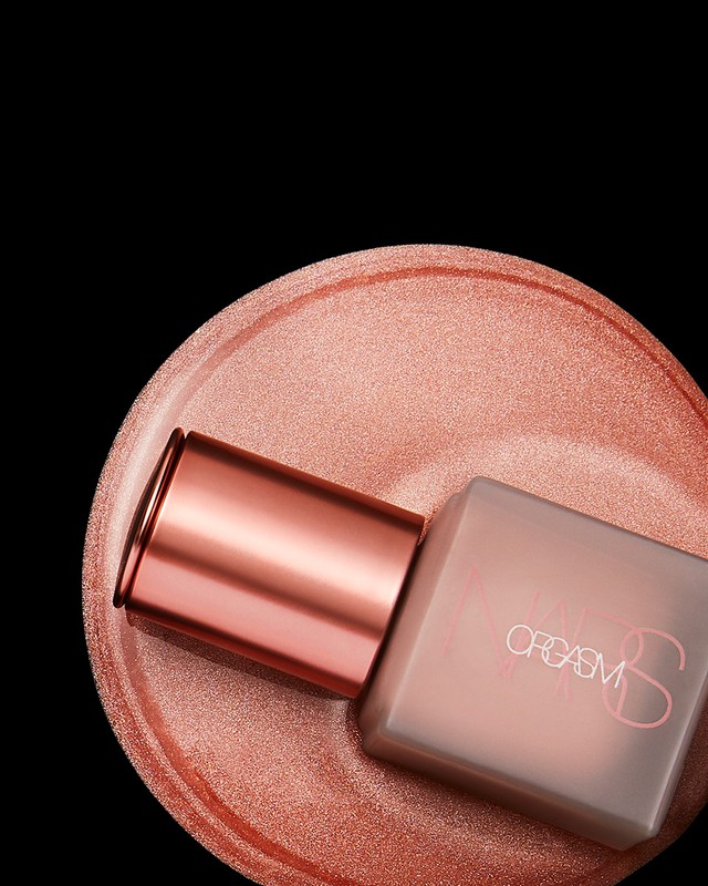 Close-up shot of a NARS Orgasm product bottle sitting on a shimmery peach-colored surface against a stark black backdrop.