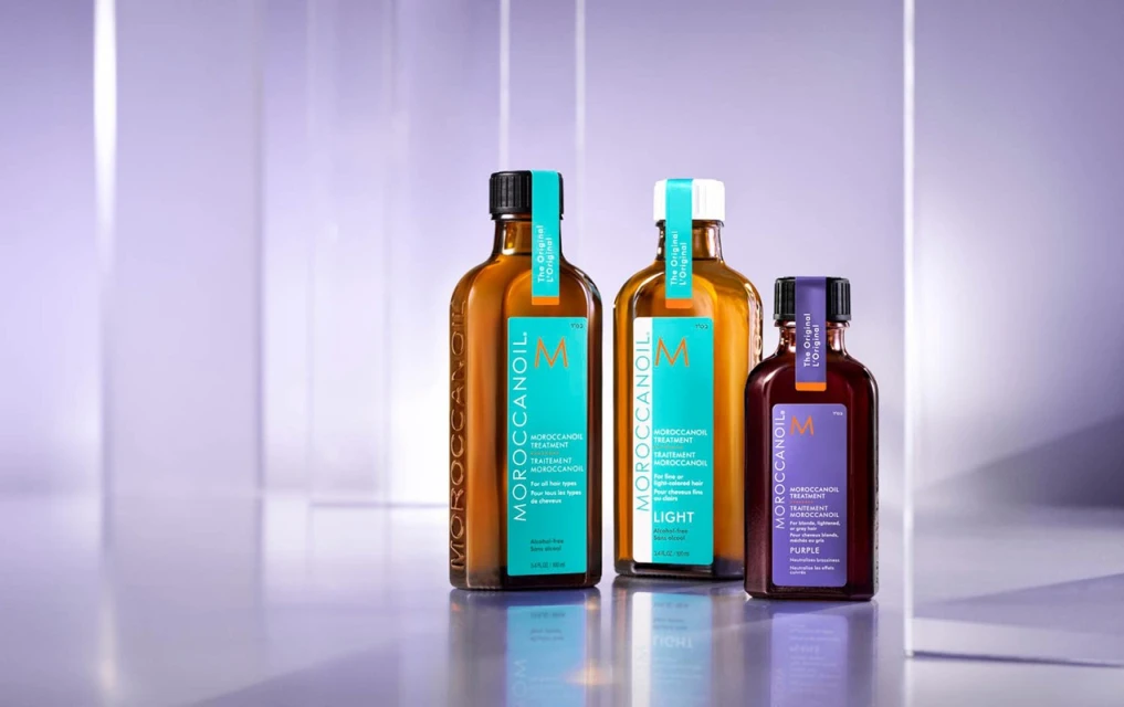 Moroccanoil hair treatment products arranged on a reflective surface against a soft, blurred purple backdrop, studio lighting.