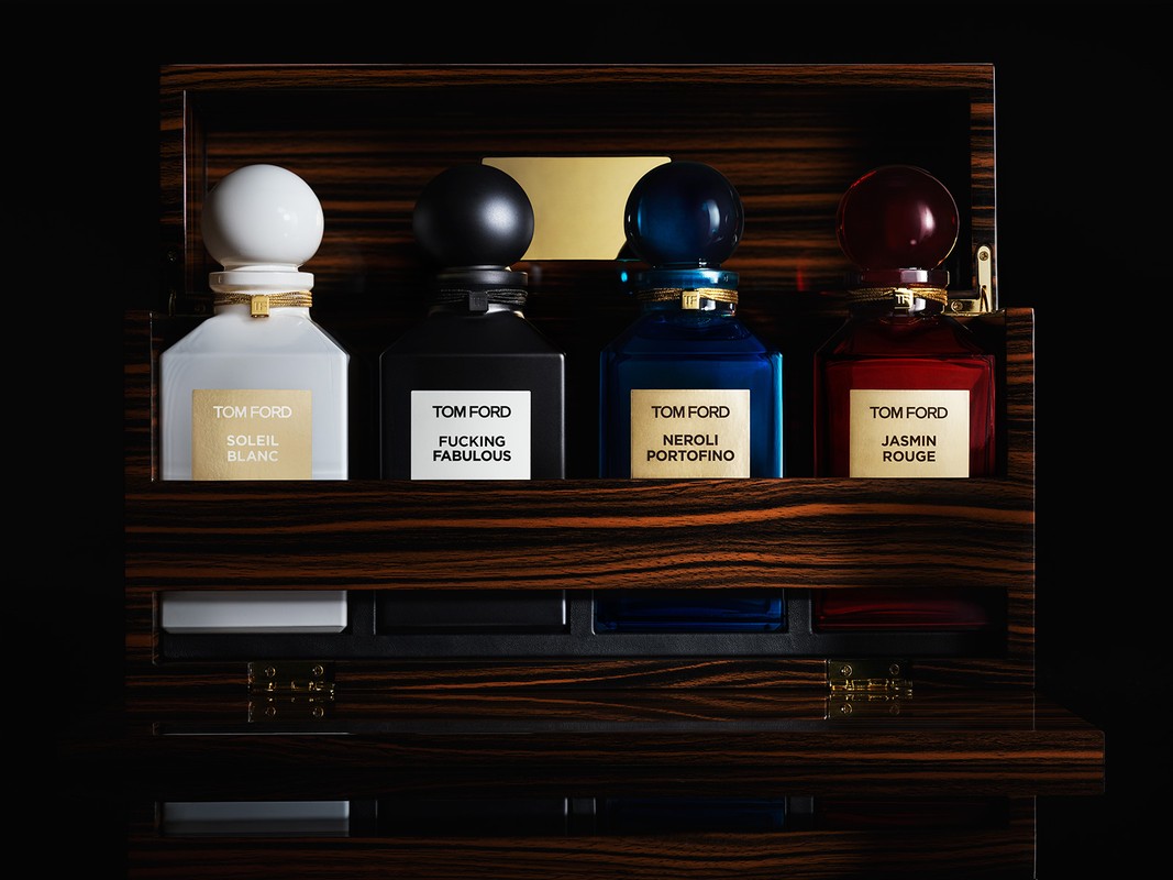 Four Tom Ford perfume bottles sit in an ornate wood case with black interior, showcasing a spectrum of colors and luxury details.