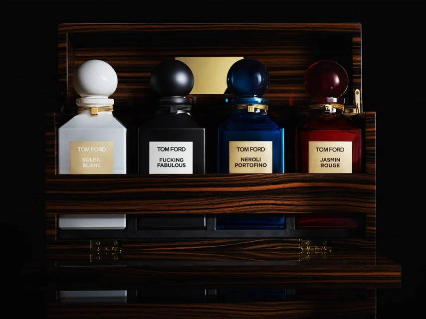 Four Tom Ford perfume bottles sit in an ornate wood case with black interior, showcasing a spectrum of colors and luxury details.