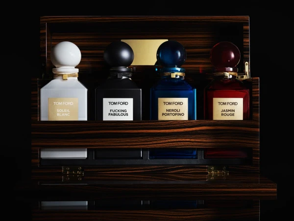 Four Tom Ford perfume bottles sit in an ornate wood case with black interior, showcasing a spectrum of colors and luxury details.
