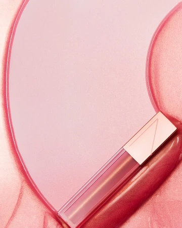 Close-up commercial product shot of a glossy cosmetic tube resting on swirling pink blush and shimmering gloss textures.