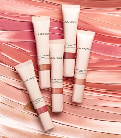 Laura Mercier Tinted Moisturizer Blush tubes are arranged on a background of blush color streaks, showcasing beauty and cosmetics.