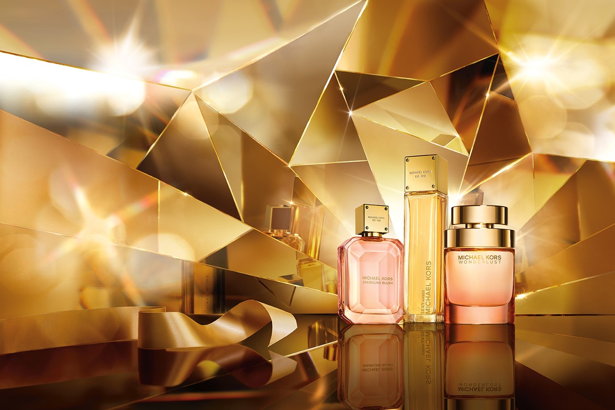 Michael Kors perfume bottles on a reflective surface, gold ribbon, and an abstract gold faceted background create a luxurious beauty image.