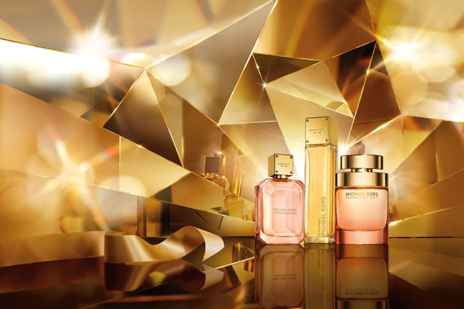 Michael Kors perfume bottles on a reflective surface, gold ribbon, and an abstract gold faceted background create a luxurious beauty image.