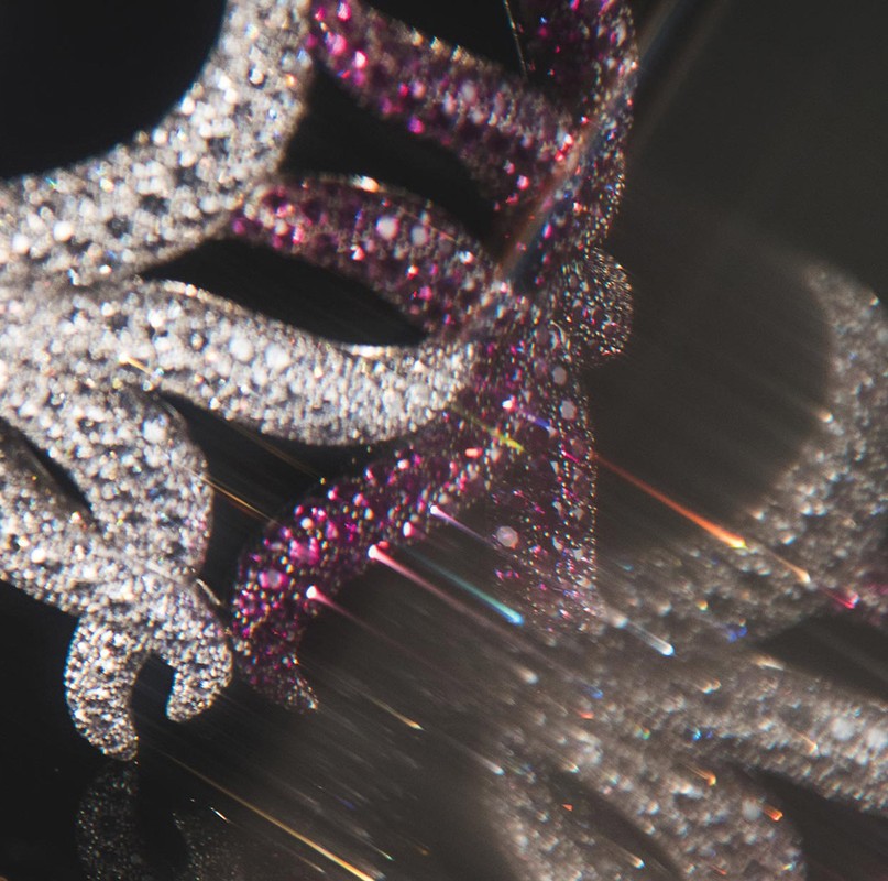Close-up of a jewelry art piece featuring a decorative design with white and pink gemstones against a dark background, sparkling with light.