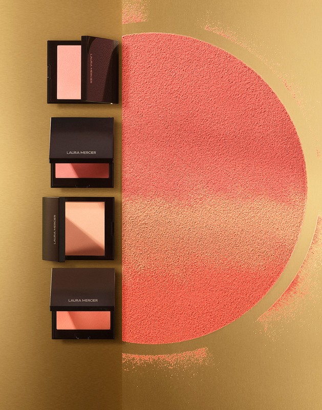 Laura Mercier bronzing powders on a gold background, with semi-circle of loose powder of the same tone, studio lighting.
