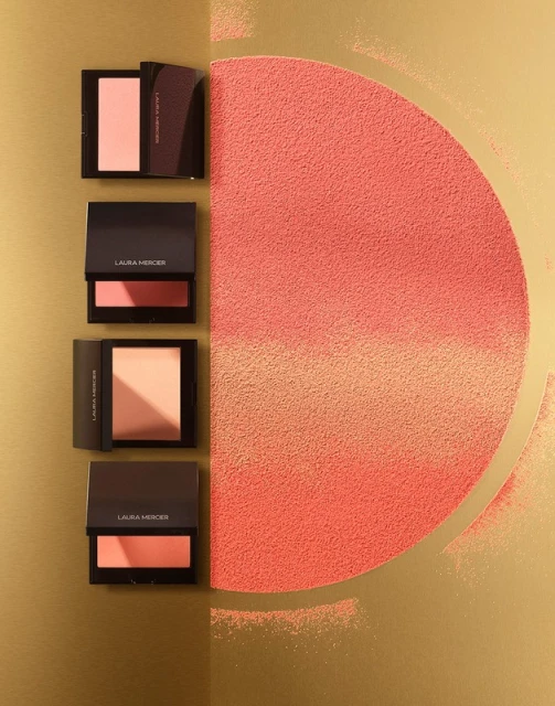 Laura Mercier bronzing powders on a gold background, with semi-circle of loose powder of the same tone, studio lighting.
