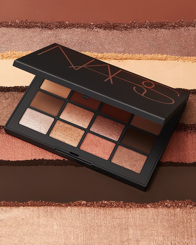 NARS eyeshadow palette with various neutral, earthy tones, set against a background of textured powders. Beauty and makeup product shot.