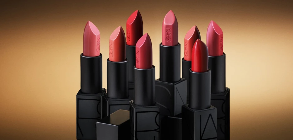 Group of NARS lipsticks in black square tubes arranged vertically against a warm golden gradient background