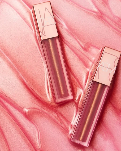 Close-up of two NARS Afterglow lip balms displayed on a glossy pink surface, showcasing a makeup product and beauty aesthetic.