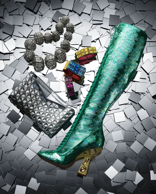 High angle studio shot of a green sequin knee-high boot, silver clutch, colorful bracelets, and a silver beaded necklace on a square tile surface.