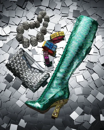 High angle studio shot of a green sequin knee-high boot, silver clutch, colorful bracelets, and a silver beaded necklace on a square tile surface.