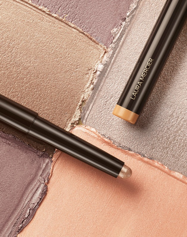 Laura Mercier eye color sticks on shimmering eyeshadow palette in peach, gold, lavender, and silver tones, makeup product shot.