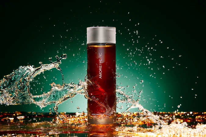 Cylindrical cosmetic bottle surrounded by dynamic water splashes against a deep green gradient background