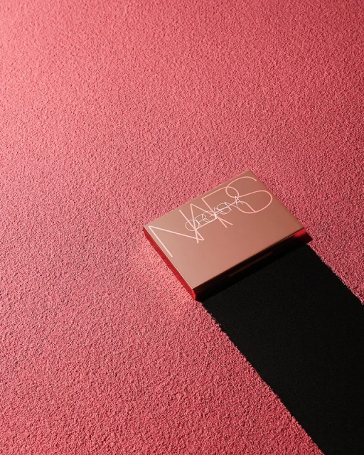 NARS eyeshadow palette on a pink textured surface with dark shadow. Beauty product shot with a cosmetic palette and background texture.