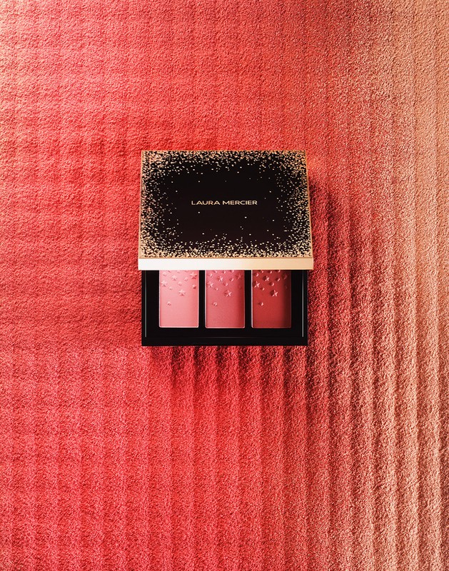 Laura Mercier blush palette on a pink striped towel background, displaying three shades of pink and coral blush colors.