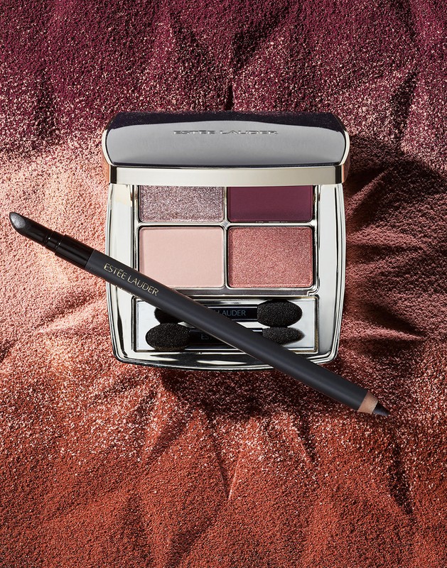 Still life of an open Estee Lauder eye shadow palette with applicator and a sparkling background in mauve and copper tones.