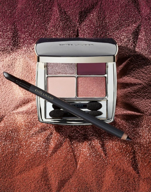 Still life of an open Estee Lauder eye shadow palette with applicator and a sparkling background in mauve and copper tones.