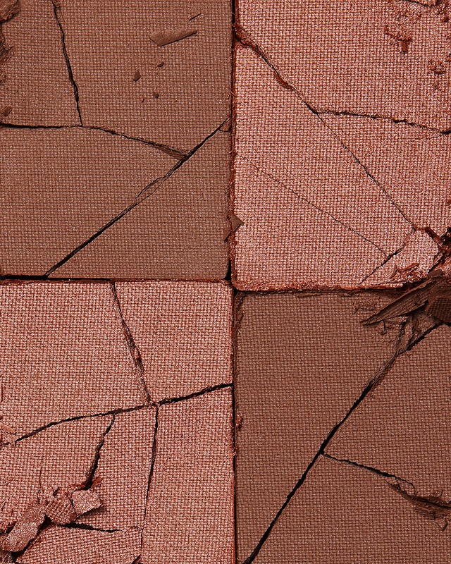 Macro shot of a cracked makeup palette with sections of bronze and pink powder showcasing a textured and damaged surface aesthetic.