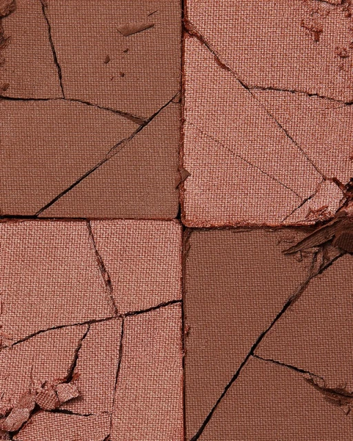 Macro shot of a cracked makeup palette with sections of bronze and pink powder showcasing a textured and damaged surface aesthetic.