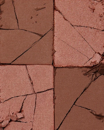 Macro shot of a cracked makeup palette with sections of bronze and pink powder showcasing a textured and damaged surface aesthetic.