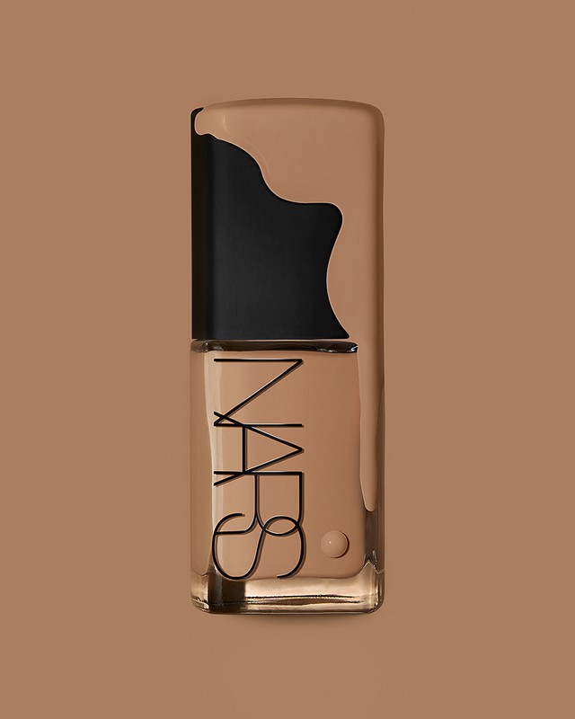 Studio shot of a NARS foundation bottle on a monochromatic tan background, with the brand logo prominently displayed on the glass.
