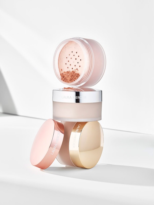 Laura Mercier translucent loose setting powder, stacked containers with gold and rose gold lids on a white backdrop.