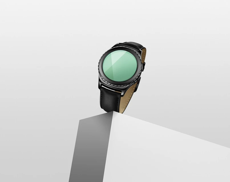 Close-up of a black smartwatch with a leather band, elevated on a white cubic pedestal against a clean, neutral background.