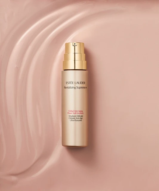 Estee Lauder Revitalizing Supreme+ emulsion bottle on a pale pink wavy background. Beauty product shot in a studio setting with soft lighting.
