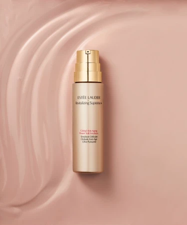 Estee Lauder Revitalizing Supreme+ emulsion bottle on a pale pink wavy background. Beauty product shot in a studio setting with soft lighting.