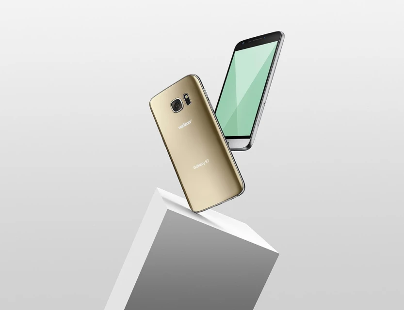 Two smartphones, one gold and one silver, float in a studio-lit scene, positioned above a white geometric block against a gradient background.