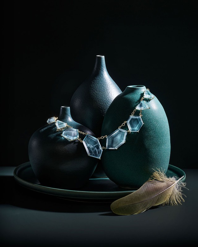 Still life photograph of three ceramic vases of different shapes and sizes sitting on a round tray, adorned with a necklace and feather.