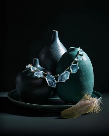 Still life photograph of three ceramic vases of different shapes and sizes sitting on a round tray, adorned with a necklace and feather.
