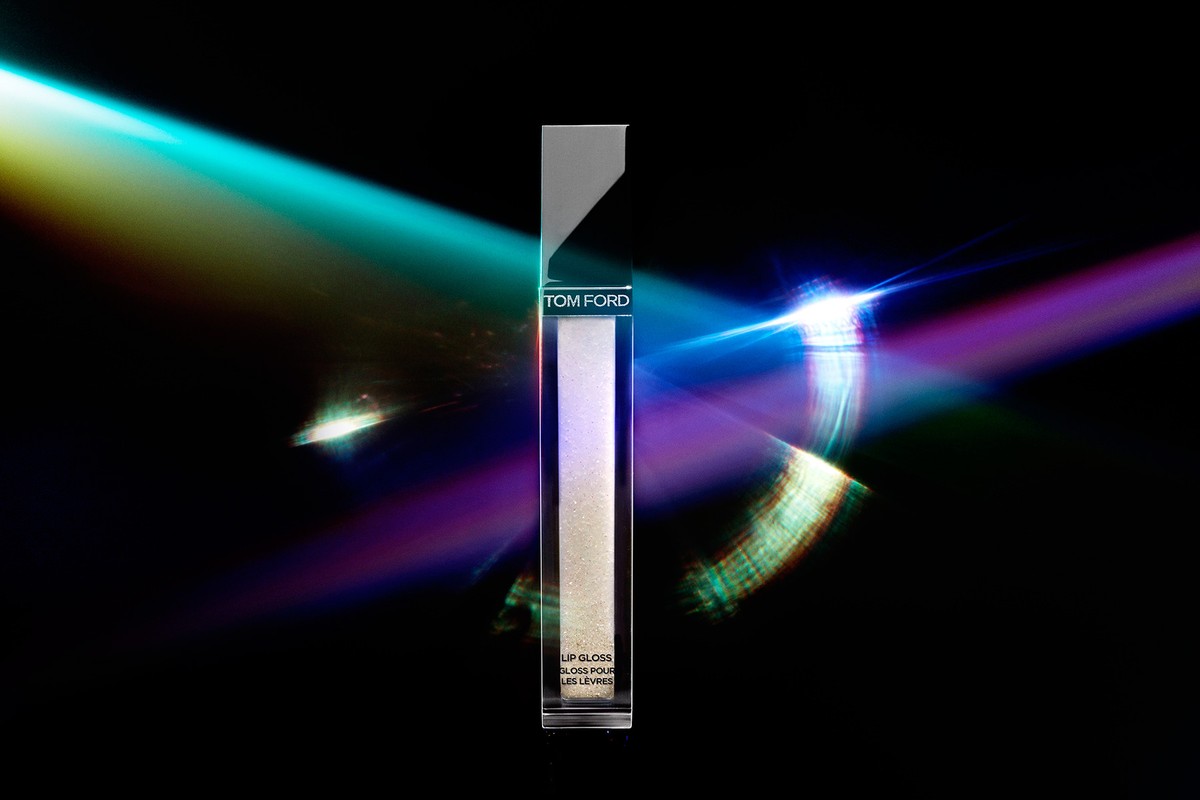 Tom Ford lip gloss tube centered vertically against a dark background with vibrant cyan and purple laser light beams cutting across the frame.
