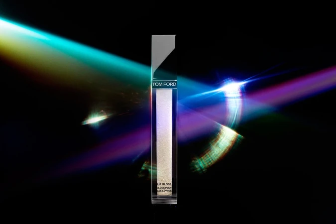 Tom Ford lip gloss tube centered vertically against a dark background with vibrant cyan and purple laser light beams cutting across the frame.