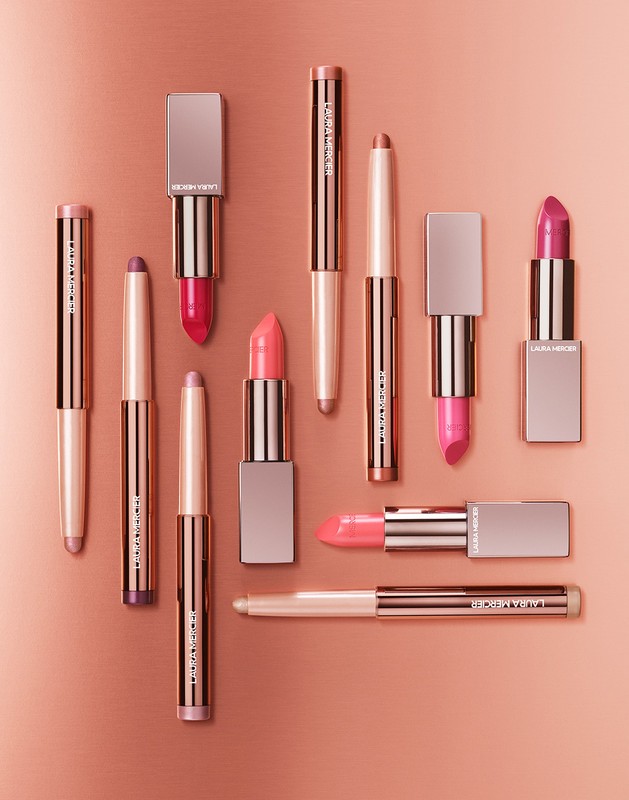 Arrangement of Laura Mercier lipsticks in various shades and formats on a gradient background, creating a beauty product display.