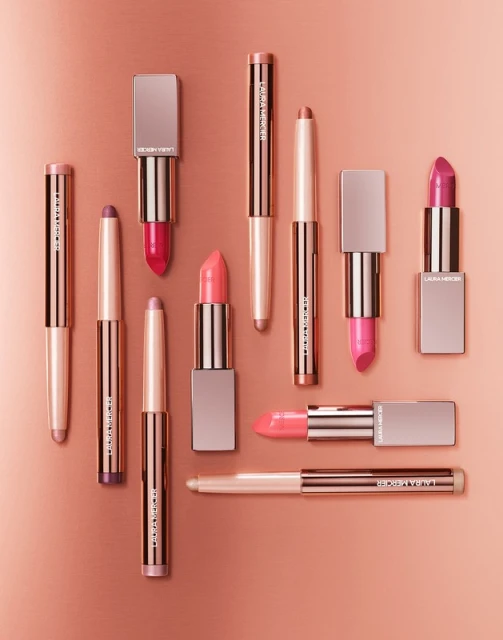 Arrangement of Laura Mercier lipsticks in various shades and formats on a gradient background, creating a beauty product display.