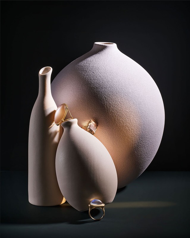 Still life shot of three vases in different sizes with gold rings on top in front of a dark background, studio lighting.