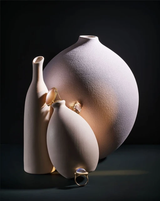 Still life shot of three vases in different sizes with gold rings on top in front of a dark background, studio lighting.