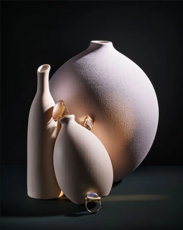 Still life shot of three vases in different sizes with gold rings on top in front of a dark background, studio lighting.