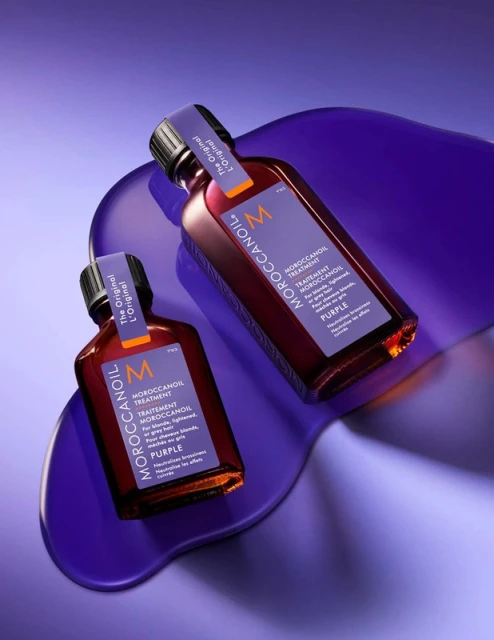 Two purple Moroccanoil hair product bottles on a vibrant purple surface, showcasing beauty and hair care.