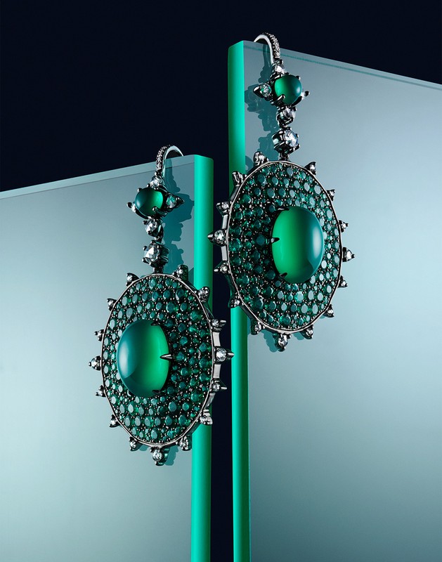 Studio shot of ornate drop earrings featuring green stones and silver metal, reflecting an elegant and luxurious aesthetic.