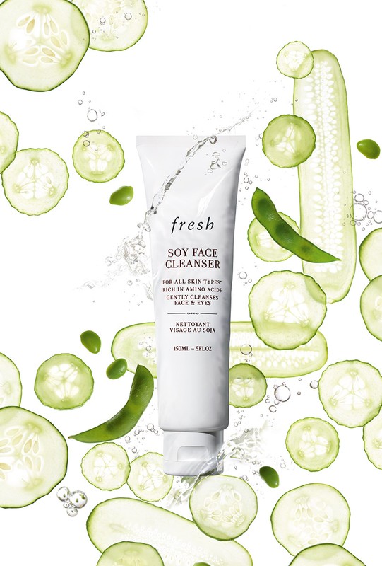 Fresh Soy Face Cleanser tube surrounded by sliced cucumbers and soybeans on a white background for a beauty and skincare product shoot.
