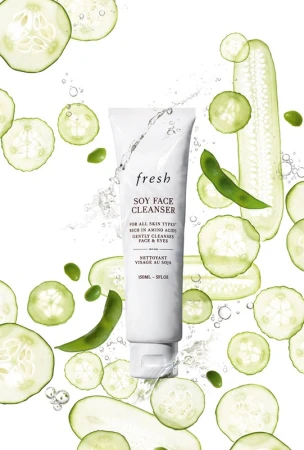 Fresh Soy Face Cleanser tube surrounded by sliced cucumbers and soybeans on a white background for a beauty and skincare product shoot.