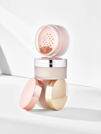 Stacked translucent setting powder jars with metallic lids arranged on a clean white surface